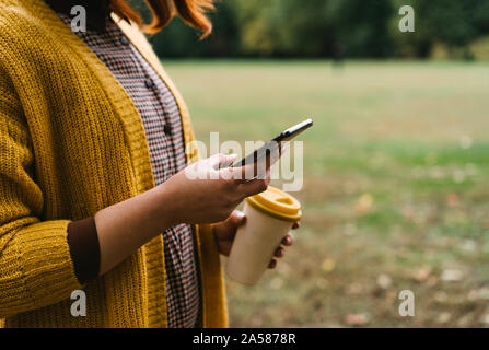 Eine rothaarige Frau im Park spazieren geht und Halten einer Bambus Schale mit Kaffee Stockfoto
