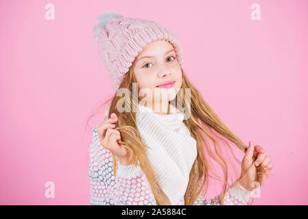 Kind lange Haare lächelnd. Mädchen tragen Strickmütze rosa Hintergrund. Winter Haar Schaden verhindern. Winter Haarpflege Tipps sollten Sie auf jeden Fall folgen. Im Winter trainieren Sie mehr zwischen den Wäschen zu gehen. Stockfoto