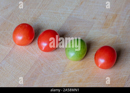 Kirschtomaten in einer Reihe auf einem Holz- choppig Board, drei rote und grüne, Symbol der biologischen Vielfalt der Natur Stockfoto