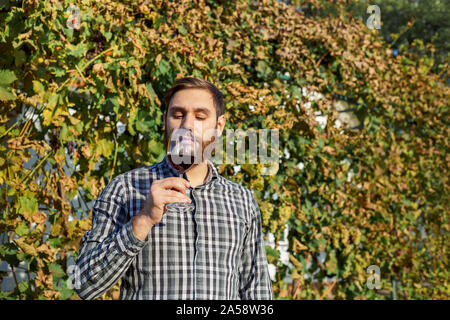 Portrait von stattlichen Winzer in seiner Hand ein Glas Rotwein und Verkostung, Kontrolle Wein Qualität beim Stehen in der Weinberge. Kleine Stockfoto