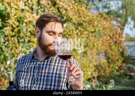 Portrait von stattlichen Winzer in seiner Hand Flasche und ein Glas Rotwein und Verkostung, Kontrolle Wein Qualität beim Stehen in der Weinberge Stockfoto