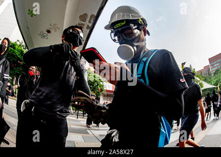 Ein Hong Kong Demonstrant das Tragen einer Gasmaske schaut auf sein Handy auf den Straßen von Hong Kong Stockfoto