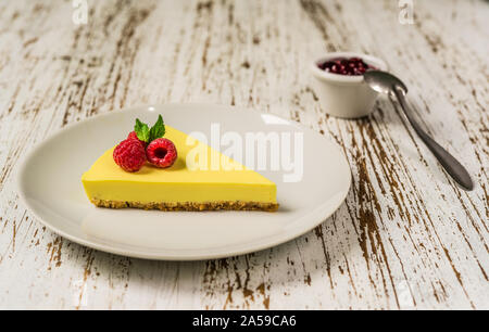Zitronen- Käsekuchen mit Himbeeren, Minze und Marmelade gegen weiße Holz Hintergrund. Stockfoto
