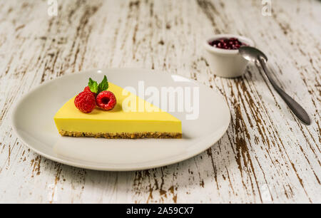 Zitronen- Käsekuchen mit Himbeeren, Minze und Marmelade gegen weiße Holz Hintergrund. Stockfoto
