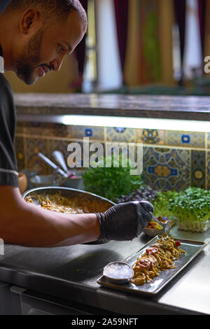 Essen Konzept. Der Chef mischt Spaghetti in einer Pfanne die Tomaten und Austern, Gericht, das in einem Restaurant. Der Prozess der Spaghetti mit Meeresfrüchten. Stockfoto