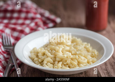 Eine Schüssel mit einfachen Teigwaren Teigwaren, billige Lebensmittel für schlechte Tage. Es ist ein Rot-weiß karierten Serviette neben die Schüssel, und eine Flasche tomatenketchup ich Stockfoto