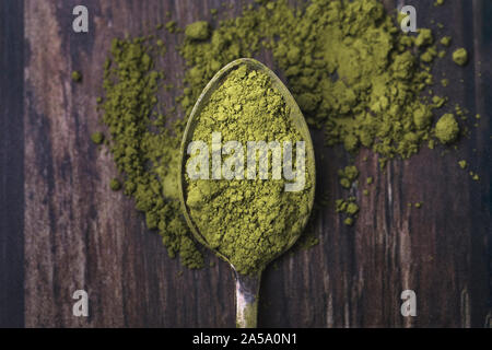 Nahaufnahme eines alten Löffel mit grünem Matcha Pulver gefüllt. Der Löffel ist auf einer alten dunklen Holztisch, und einige Pulver auf den Tisch verschüttet. T Stockfoto
