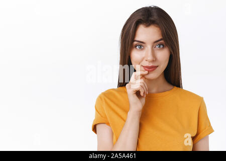 Nachdenklich, gut aussehende wagemutige junge moderne Frau im gelben T-Shirt lächelt frech und kreativ, berühren Lippe haben interessante Idee, mit Promo fasziniert Stockfoto