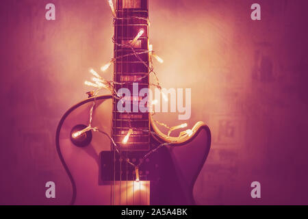White Jazz Gitarre und Weihnachtsschmuck auf dem dunklen Hintergrund. E-Gitarre mit beleuchtete Girlande auf dunklem Hintergrund. Geschenk Gitarre klassische Form Stockfoto
