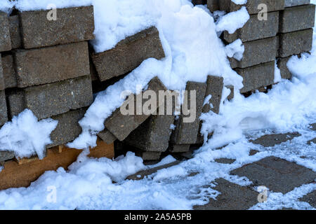Pflastersteine warten im Winter verwendet werden. Sie sind unter Schnee bedeckt. Einige der Steine fielen von dem Haufen. Stockfoto