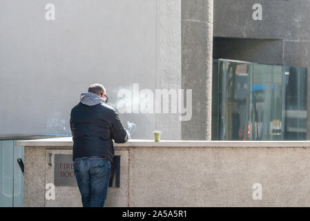 Ein weißer Mann mittleren Alters mit Blick weg von der Kamera, rauchen und trinken Kaffee allein außerhalb einer Stadt Gebäude in Sydney, Australien Stockfoto