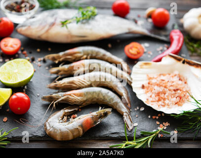 Frische rohe Garnelen, dorado Fisch und Gewürzen auf schwarzen Stein Hintergrund Stockfoto