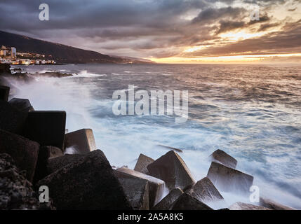 Einen malerischen Sonnenuntergang mit Wellen gegen die Felsen, Puerto de la Cruz, Teneriffa, Spanien. Stockfoto