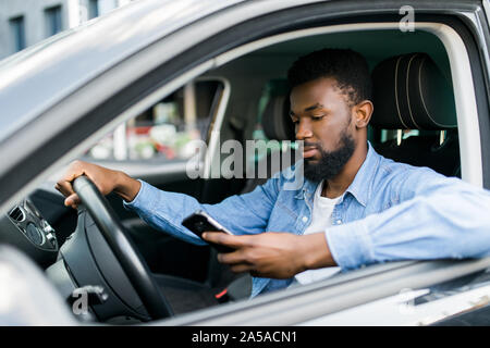 In Car-Ansicht des jungen männlichen Afroamerikaner hält sein Handy Stockfoto