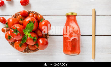 Roh Bio Tomaten in gewebter Korb mit Saft Flasche auf weiße hölzerne Tischplatte - gesundes Essen und Trinken Konzept Stockfoto