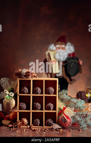 Schokolade Bonbons in Holzkiste und Weihnachtsschmuck. Gebrochene Stücke Schokolade, Zimtstangen, Sternanis und Kaffeebohnen auf braunem Grund. Co Stockfoto