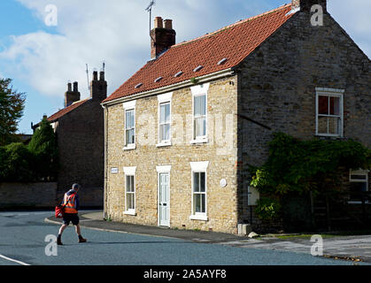 Briefträger auf seiner Runde im Dorf nördlich Newbald, East Yorkshire, England, Großbritannien Stockfoto