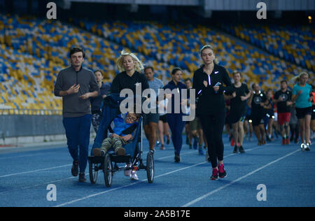 Gruppe von Menschen, die an den Anschlüssen des Stadions, in der Mitte - Frau laufen und Schieben des Rollstuhls mit Deaktiviert (zerebrale Lähmung) Junge. Oktober Stockfoto