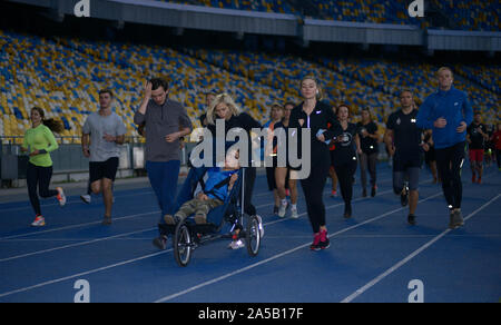 Gruppe von Menschen, die an den Anschlüssen des Stadions, in der Mitte - Frau laufen und Schieben des Rollstuhls mit Deaktiviert (zerebrale Lähmung) Junge. Oktober Stockfoto