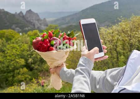 Mädchen nimmt einen Blumenstrauß aus roten Blüten und Früchte auf einer Kamera des Telefons. Stockfoto