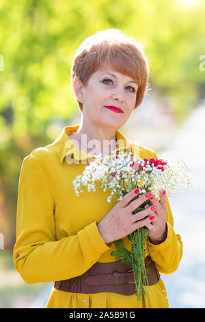 Schöne Frau im Alter zwischen 55-65 Jahre hält Die Zustellung der Blumen in den Händen Stockfoto
