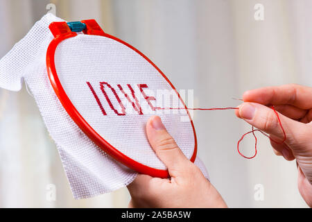 Hände von Frau kreuz Sticken - ein Wort Liebe Stich Stockfoto