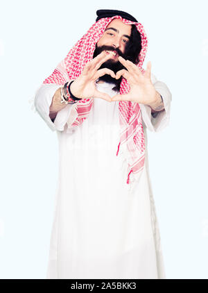Arabian Business Mann mit langem Haar zu tragen traditionelle Kufiya Schal in der Liebe mit Herz und mit Hand lächelnd. Romantische Konzept. Stockfoto