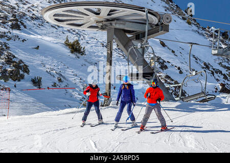 Pyrenäen, ANDORRA - Februar 13, 2019: Drei der Skifahrer in bunten Kleidern gehen weg vom Sessellift an der Spitze. Schneebedeckten Hang und Metallkonstruktionen Stockfoto