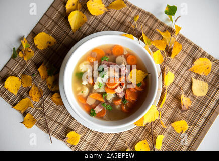 Ein overhead Foto eine Platte eines Pilzsuppe mit Steinpilzen, frische Petersilie, Blumenkohl, Karotten, auf einem dunklen Serviette Herbst Blätter Hintergrund Textur Stockfoto