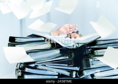 Verzweifelte Frau hinter hohen Stapel von Ringbüchern und viele Papiere sind Fliegen um im Büro, Konzept der Überforderung und der zunehmenden wor Stockfoto