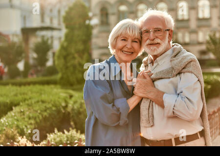 Liebe ist Leben. Portrait von fröhlichen Happy senior Paar kleben aneinander und halten sich an den Händen während im Park zusammen Stockfoto