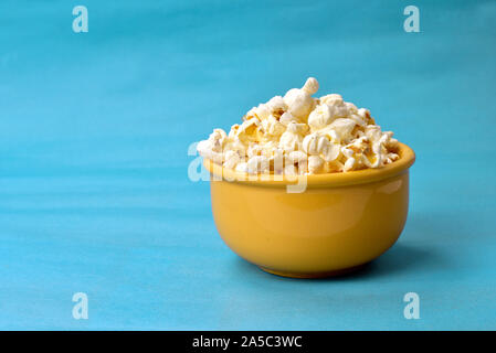 Popcorn in Schüssel mit Rosa unten mit Mais neben auf blauem Hintergrund Stockfoto