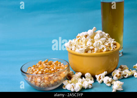 Popcorn in Schüssel mit Rosa unten mit Mais neben auf blauem Hintergrund Stockfoto