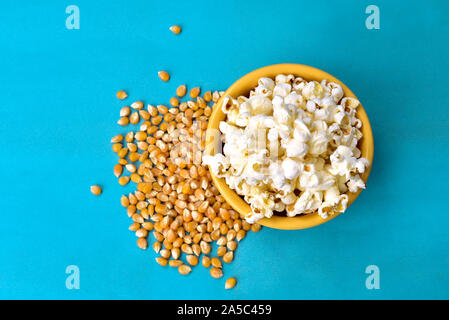 Popcorn in Schüssel mit Rosa unten mit Mais neben auf blauem Hintergrund Stockfoto