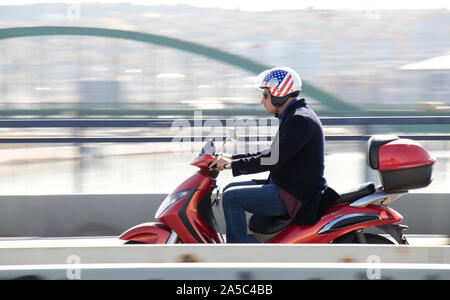 Belgrad, Serbien - Oktober 16, 2019: Ein Mann in Blazer und Jeans tragen Amerikanische Flagge Helm, rot Roller über die Stadt Street Bridge in Besetzt Stockfoto