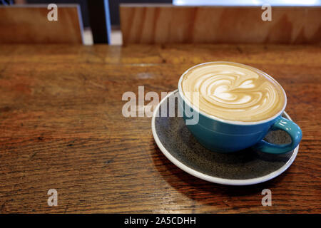 Close Up und Top Aussicht auf schöne latte Kunst mit Herz Muster auf der Oberseite des Kaffee Cappuccino aus weisser Keramik Schale auf Holz Zähler in Coffee Bar. Stockfoto