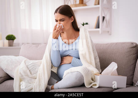 Schwangere Frau blasen Nase im Gewebe sitzt auf einem Sofa indoor Stockfoto