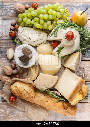 Ansicht von oben verschiedene köstliche Käsesorten, Nüsse, Früchte, würzige Kräuter und Zwiebeln baguette auf einem urigen Hintergrund. Vertikaler Dampfstoß Stockfoto