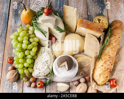 Verschiedene köstliche Käsesorten, Nüsse, Früchte, würzige Kräuter und Zwiebeln baguette auf einem urigen Hintergrund. Stockfoto