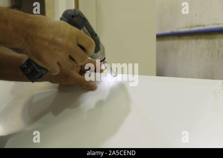 Männliche Hand arbeitet auf weißem Sperrholz mit einem kleinen Bohrer Stockfoto
