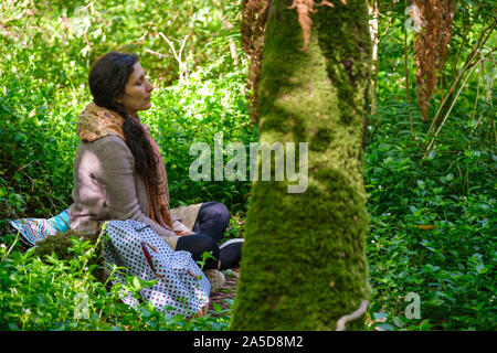 Frau sitzt im Wald mit den Augen bei einem Wald baden Sitzung geschlossen Stockfoto