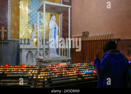 Frau, die zur Statue der Jungfrau Maria betet, nachdem sie eine Kerze in der Basilika unserer Lieben Frau vom Rosenkochen im Heiligtum unserer Lieben Frau von Lourdes, Frankreich, angezündet hat Stockfoto