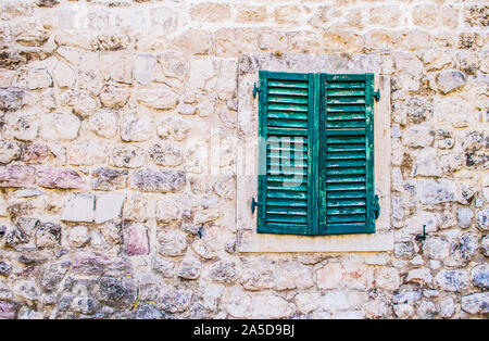 Alte Steinmauer mit geschlossenen verwitterten hölzernen Fensterläden Fenster. Stockfoto
