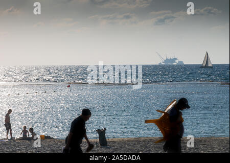 DOR STRAND, Israel/18 OKT 2019: Badegäste am Strand als Segelboot an der Vorderseite der ökologisch umstrittene offshore Bohrinsel Stockfoto