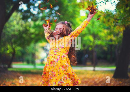 Wenig lächelnde Mädchen spielen mit Blätter im Herbst in einem Sunshine Park Stockfoto