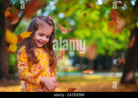 Herbst Park und glückliche kleine Mädchen spielen mit gefallenen Baum Blätter Stockfoto