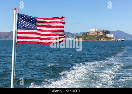 Das Sternenbanner Flagge von einem Boot mit Alcatraz Island aus Fokus hinter. Stockfoto