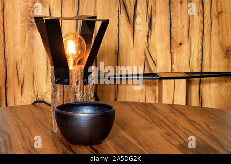 Original Lampe aus einem alten Bar aus Holz und einem metallschutz Grill rund um die Lampe und einem schwarzen Ton Schüssel auf einem Holztisch und eine alte Risse im Holz- ba Stockfoto