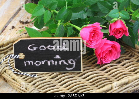 Guten Morgen auf mini Tafel mit wilden pick Rosen auf wicker Oberfläche geschrieben Stockfoto