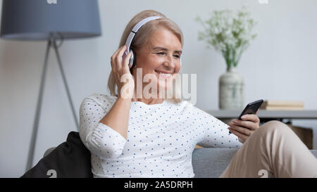 Lächelnd reife Frau tragen drahtlose Kopfhörer im Bildschirm "Telefon" suchen Stockfoto